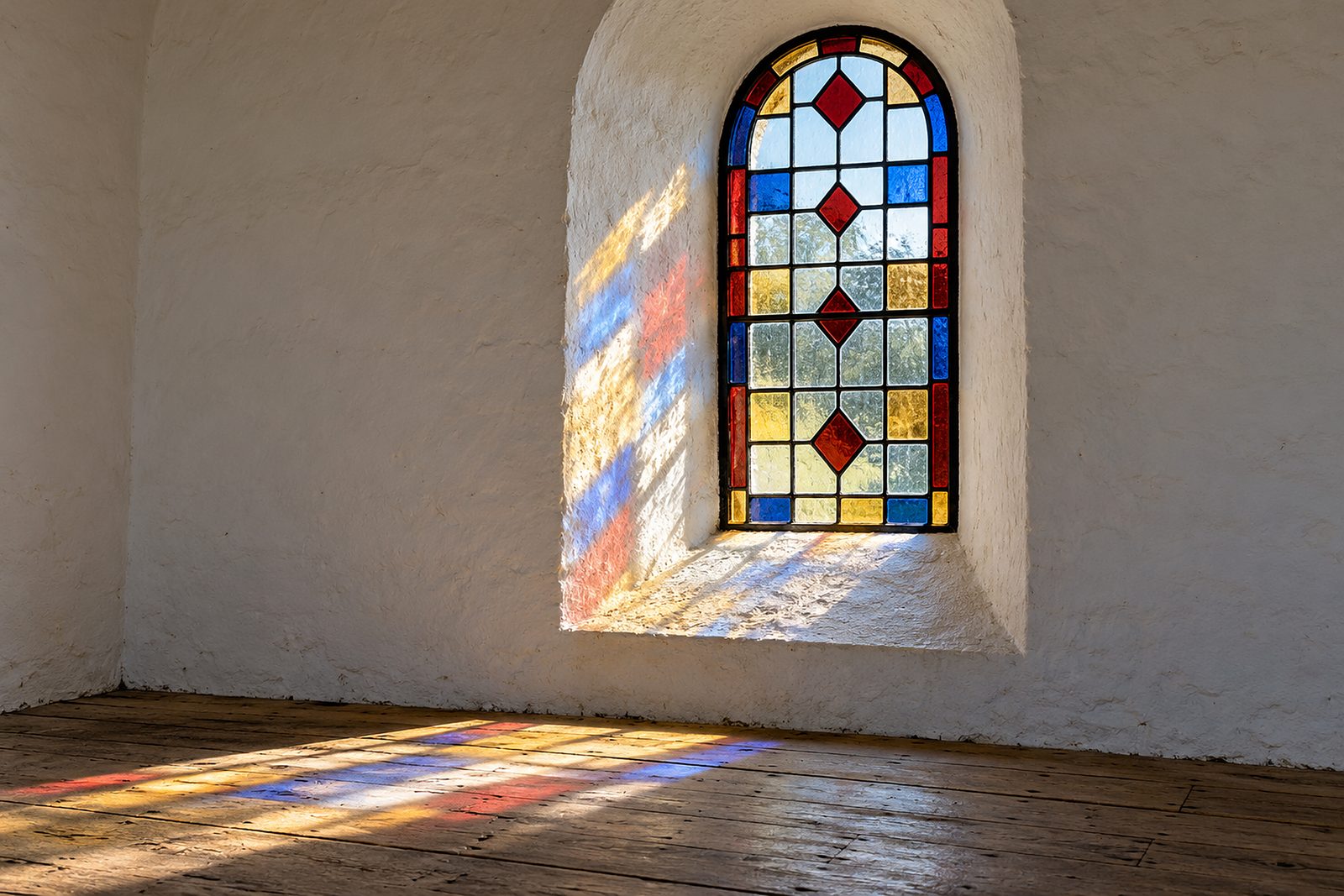 Bleiverglastes Rundbogenfenster in einer weiß gekalkten Kapelle, die Sonne wirft farbige Flecken auf Putz und Dielen (KI-Illustration)